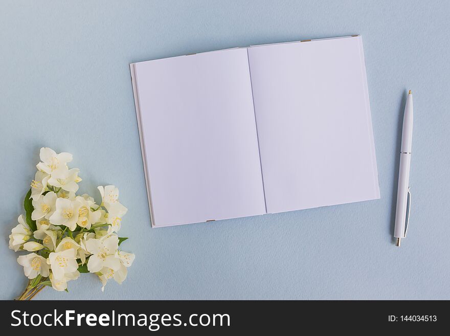 Mockup notebook with white jasmine flowers and light blue background  empty space for your text, top view