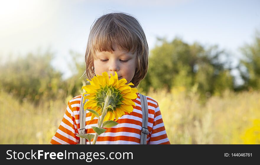 Happy boy with sunflower outdoors. Children play in garden.