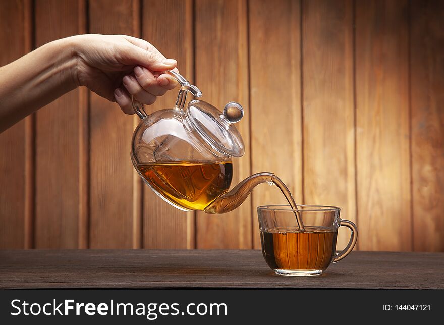 Woman hand poured cup of tea on a wooden table from a teapot.