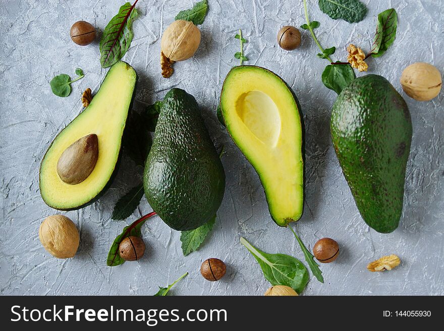 Avocado cut in half lies on a gray concrete background surrounded by nuts and green salad leaves ,snack Keto diet