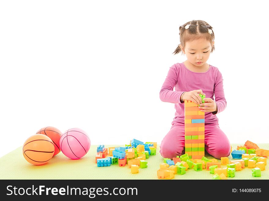 Portrait of cute little Asian girl in purple t-shirt and pants happily standing on green yoga mat holding multi-colorblocks toy and plastic baby toy balls on isolated white background. Portrait of cute little Asian girl in purple t-shirt and pants happily standing on green yoga mat holding multi-colorblocks toy and plastic baby toy balls on isolated white background