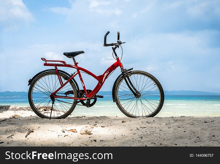 Red vintage bicycle on white sand beach over blue sea and clear blue sky background, spring or summer holiday vacation concept. Bicycle parked by the sea