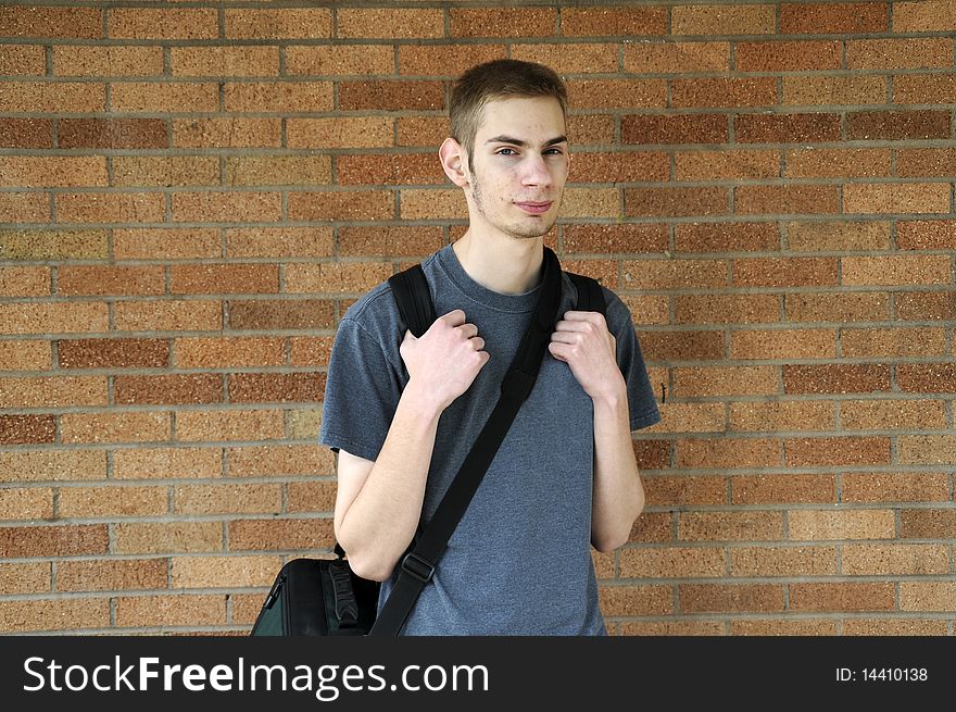 Young caucasian male looks at the camera with his backpack on against a wall. Young caucasian male looks at the camera with his backpack on against a wall.