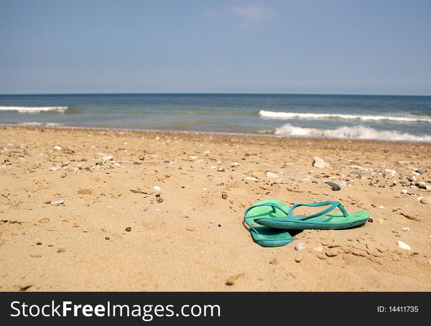 A pair of turquoise-green flipflops on a sandy and stony beach. A pair of turquoise-green flipflops on a sandy and stony beach