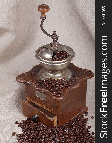 Antique coffee grinder with fried beans over canvas