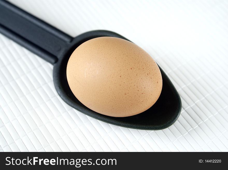 Raw egg on a white background and a spoon.