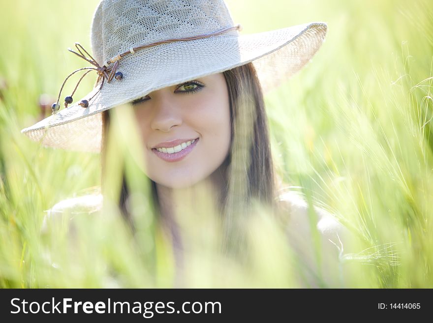 Young beautiful girl with hat staring at camera among green wheat. Young beautiful girl with hat staring at camera among green wheat.