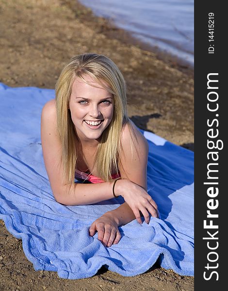 A woman laying and smiling while she is on a blue blanket on the beach. A woman laying and smiling while she is on a blue blanket on the beach.