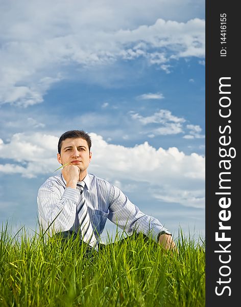 A young businessman relaxing in a meadow on a very cloudy background