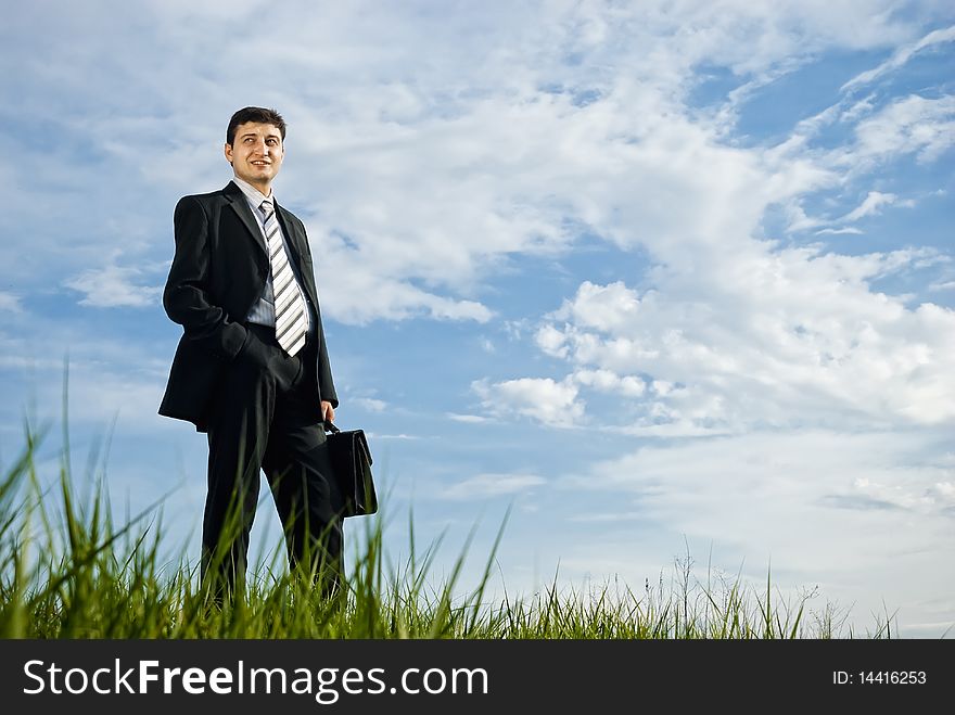Young businessman is staying outdoors with briefcase in his hand on a very cloudy background