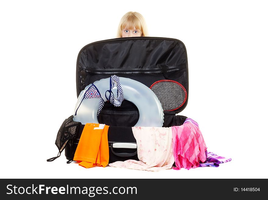 Girl surprise peeking out behind suitcase with things for a vacation isolated on white. Girl surprise peeking out behind suitcase with things for a vacation isolated on white