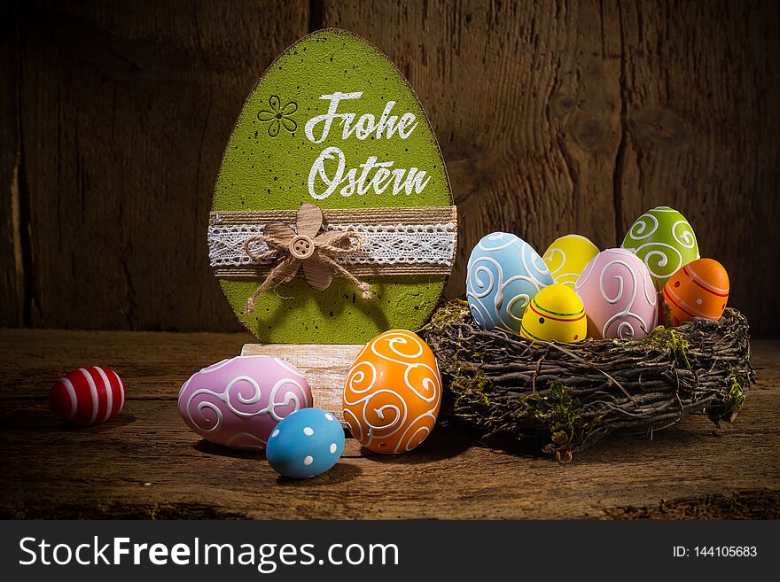 German greetings Frohe Ostern  english translation happy easter  Colorful painted eggs in birds nest basket on rustic wooden old  greeting card background