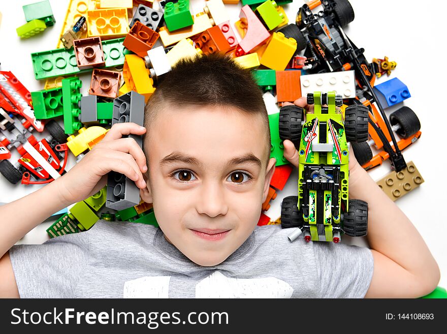 Joyful Little boy playing with a lot of colorful plastic blocks indoor, lying on the floor among the toys, built a machine from the designer and shows it. Joyful Little boy playing with a lot of colorful plastic blocks indoor, lying on the floor among the toys, built a machine from the designer and shows it.