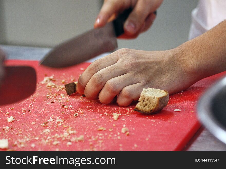 Man hands cutting bread for crutons on red cutting doard. Preparing bread for roasting croutons. Man hands cutting bread for crutons on red cutting doard. Preparing bread for roasting croutons