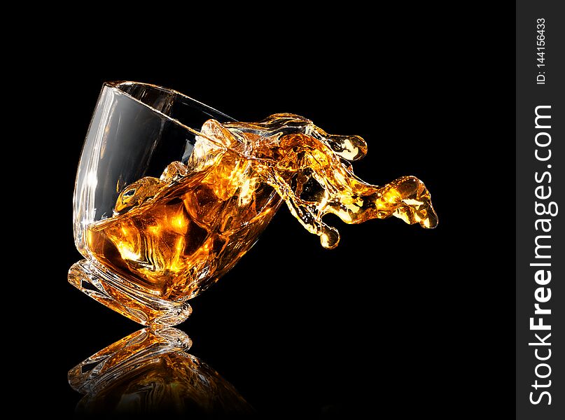 Splash of whiskey with ice cubes in glass on black background. Splash of whiskey with ice cubes in glass on black background