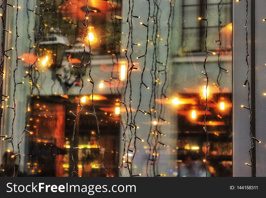 Reflection of architecture, lights in the Christmas, New Year`s shop windows, on windows, windows, wet asphalt . Selected focus.
