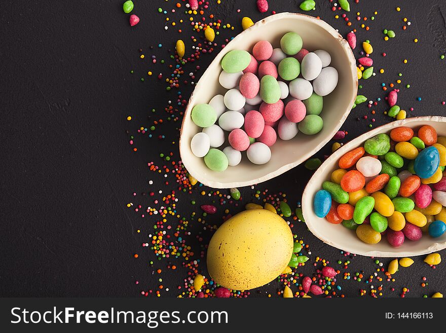 Chocolate eggs and scattered colorful candies on dark background, copy space. Chocolate eggs and scattered colorful candies on dark background, copy space