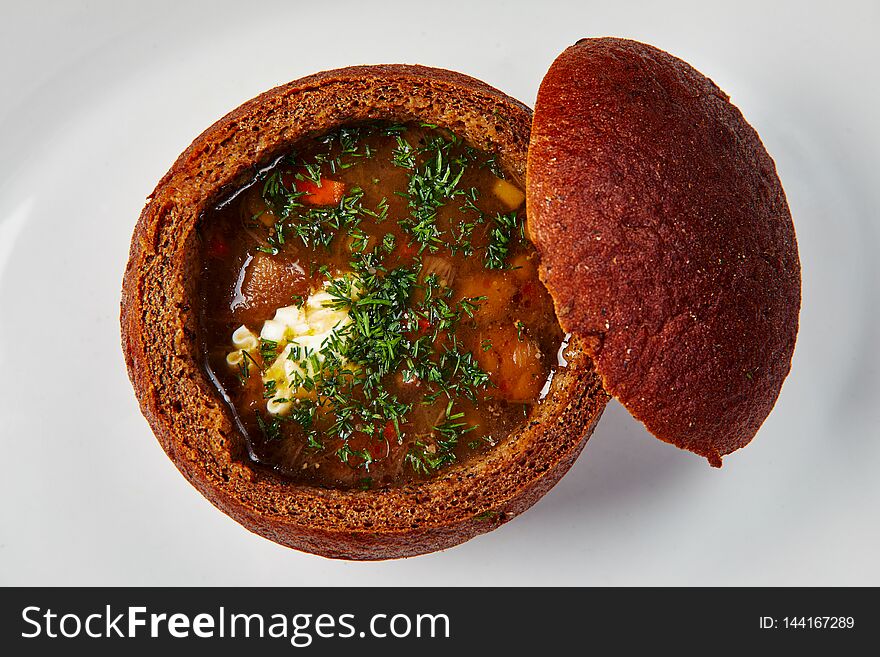 Restaurant food. Rustic closeup of red the soup in bread on white background.