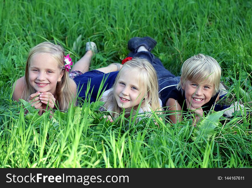 Three kids lying on green grass in park.