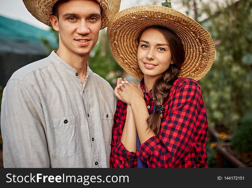 Guy And Girl Gardeners In A Straw Hats Stand Together In Garden On A Sunny Day.