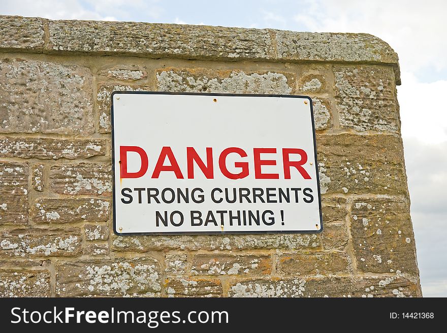 An image of a prominent warning sign on a sea wall indicating that because of strong currents in the sea it is dangerous to bathe. An image of a prominent warning sign on a sea wall indicating that because of strong currents in the sea it is dangerous to bathe.