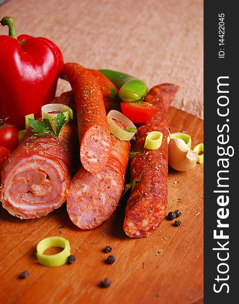 Various sausages on wooden plate with vegetables