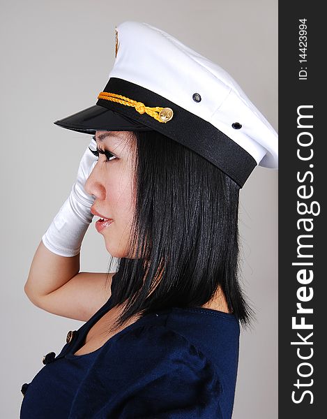 A young pretty Asian woman, in a sailor uniform and white gloves and sailor a cap , in an portrait, standing saluting in the studio for light gray background. A young pretty Asian woman, in a sailor uniform and white gloves and sailor a cap , in an portrait, standing saluting in the studio for light gray background.