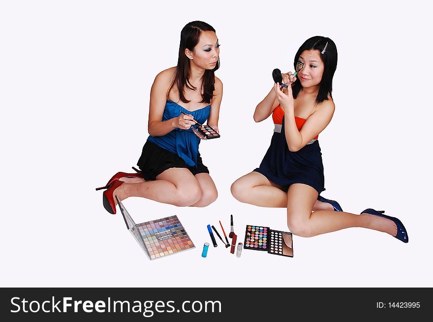 Two Asian woman sitting on the floor in the studio and helping each other with the makeup for the next photo shoot, for light gray background. Two Asian woman sitting on the floor in the studio and helping each other with the makeup for the next photo shoot, for light gray background.