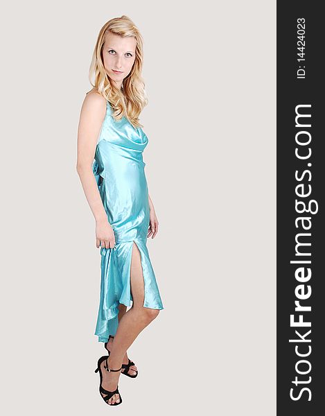 A beautiful tall blond woman in an light blue long dress and high heels standing from the site in the studio for a portrait, on light gray background. A beautiful tall blond woman in an light blue long dress and high heels standing from the site in the studio for a portrait, on light gray background.