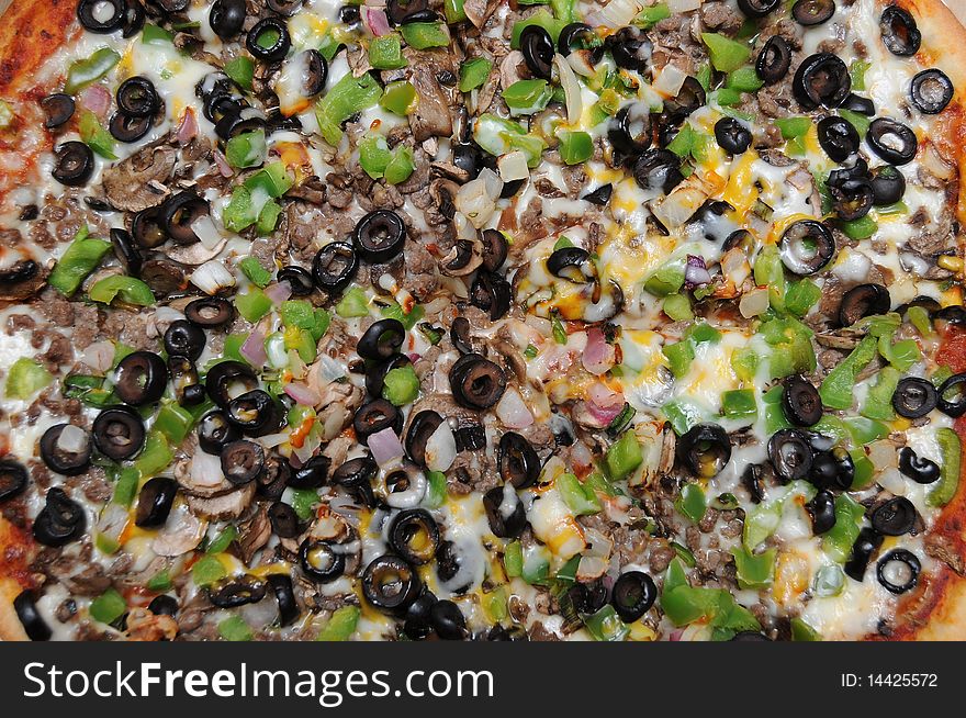 Pizza with black olives, green pepper, mushrooms, cheese, and ground beef hamburger meat with purple onions.