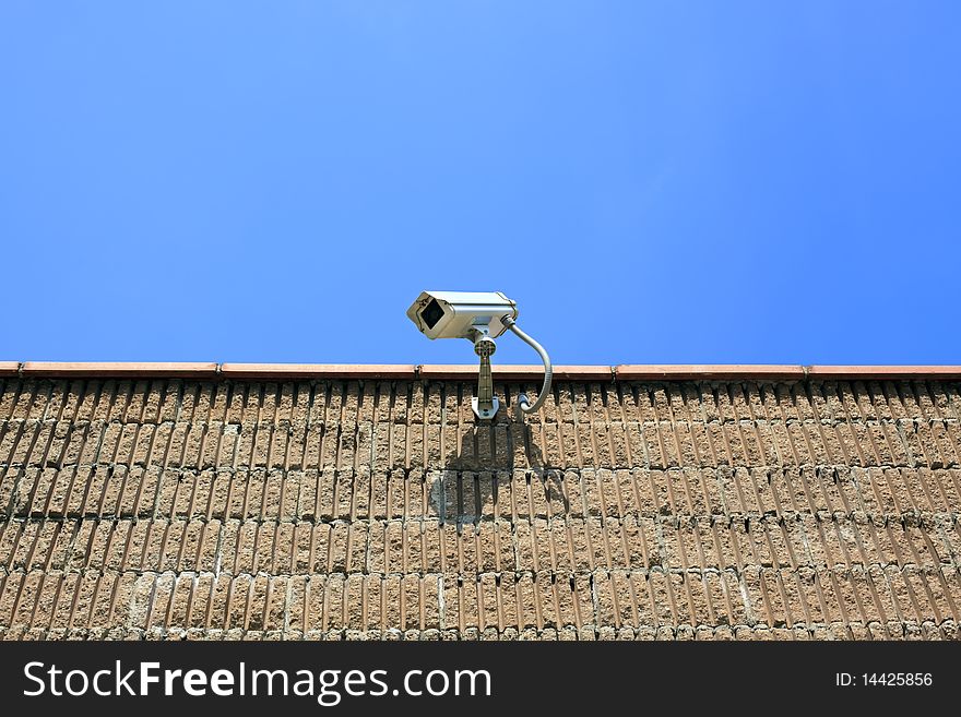 Security camera on a wall with clear blue skies behind it