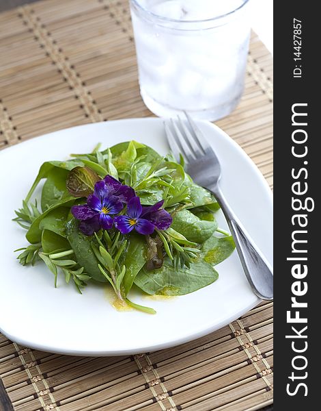 A fresh spinach salad with an edible flower garnish. A fresh spinach salad with an edible flower garnish.