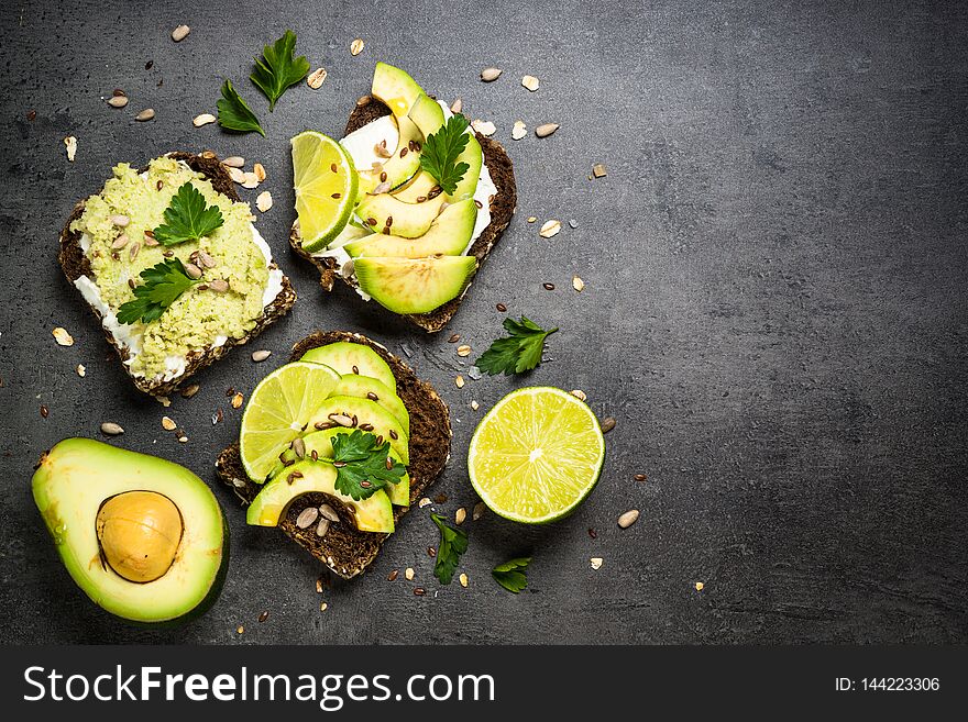 Sandwiches with avocado and cream cheese with grain bread and seeds. Black slate background, top view. Sandwiches with avocado and cream cheese with grain bread and seeds. Black slate background, top view.