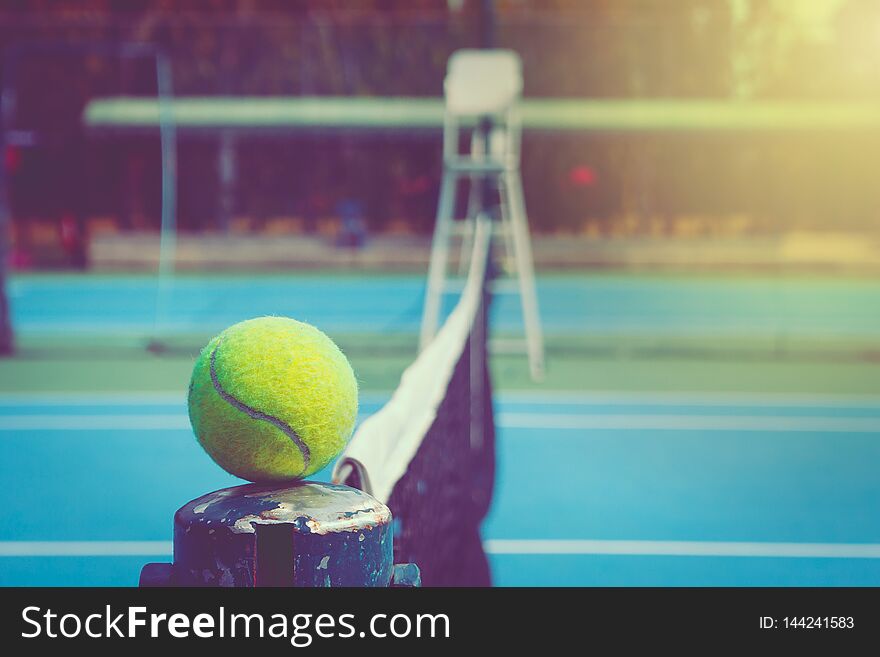 Green ball place on net pole and black net of outdoor blue tennis hard court in public park. Selective focus