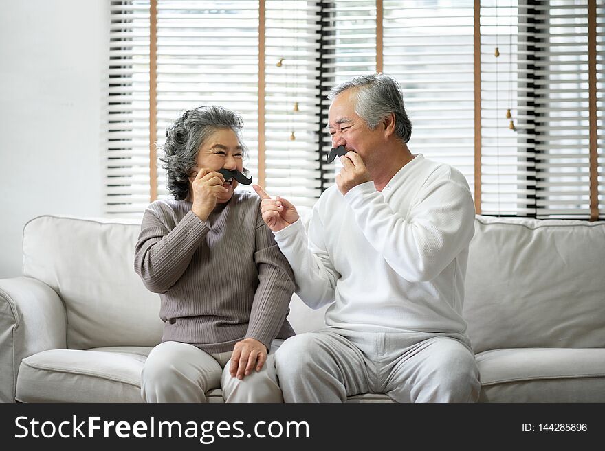 Senior Couple Are Sitting On Sofa And Playing Paper Mustaches