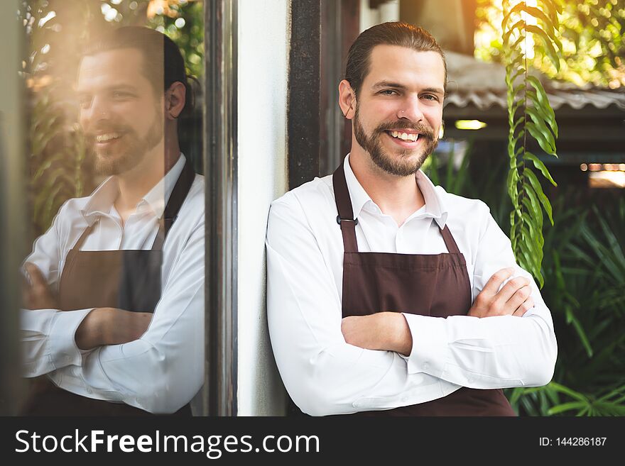 Successful Male Barista standing on front of the coffee shop. Portrait of Beard man with arms crossed
