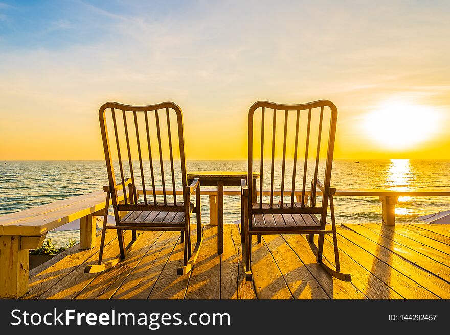 Empty wood chair and table at outdoor patio with beautiful tropical beach and sea at sunrise or sunset background for vacation and travel