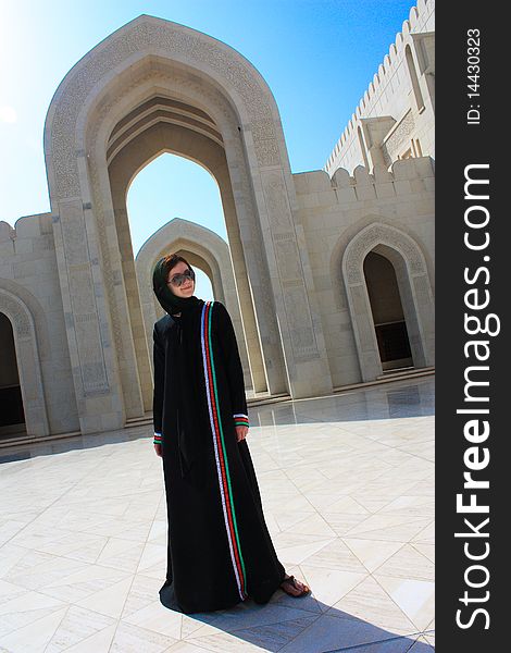 Young woman dressed up in traditional long black omani dress standing in the yard of a mosque. Young woman dressed up in traditional long black omani dress standing in the yard of a mosque