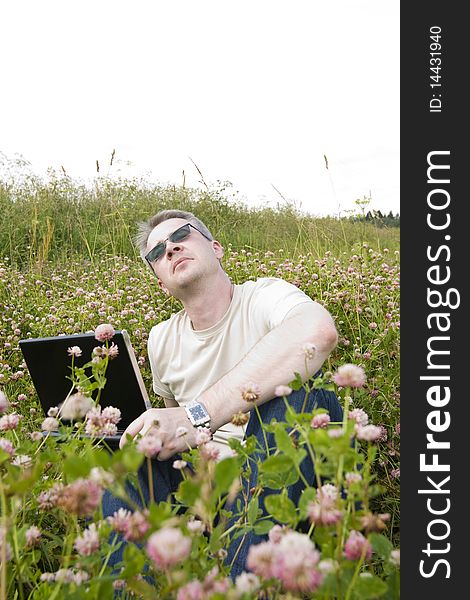 Thoughtful man with laptop on meadow