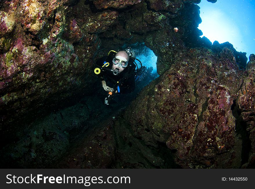 Male scuba diver swimms through a swim through underwater. Male scuba diver swimms through a swim through underwater