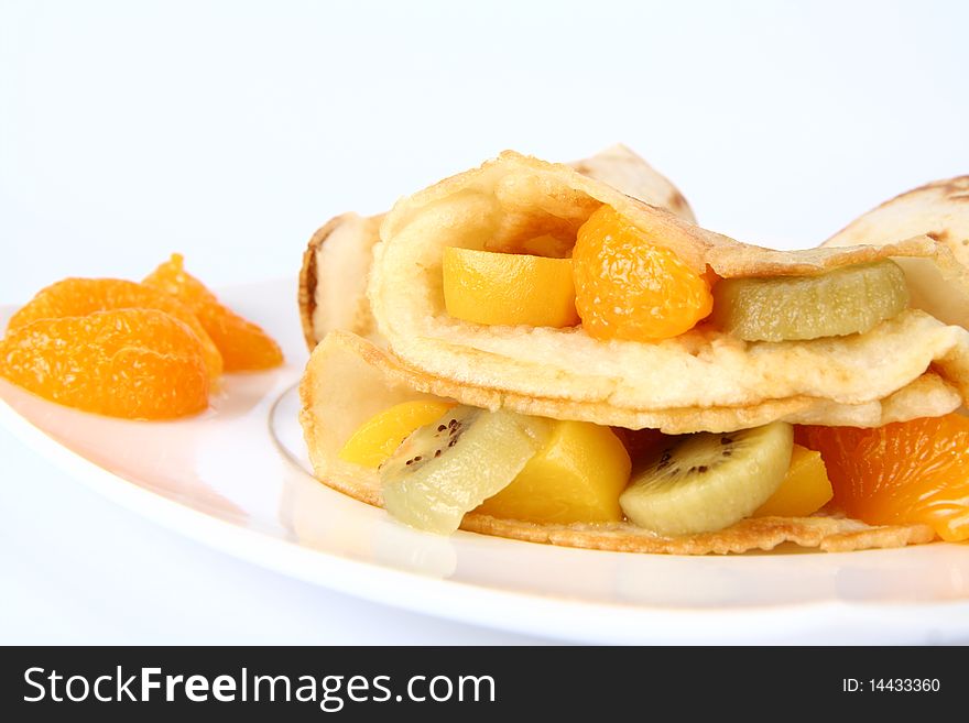 Pancakes stuffed with fruit (peach, kiwi, mandarin) on a plate decorated with fruit in close up