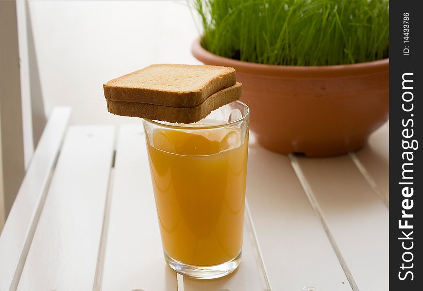 Glass of orange juice with toasts on a white board