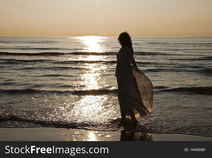 A happy woman standing on the beachin a loose dress, enjoying the beautiful sunset. A happy woman standing on the beachin a loose dress, enjoying the beautiful sunset.