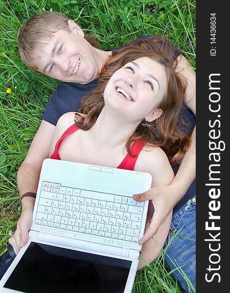 Young pair, on nature with a laptop, lyings on a grass