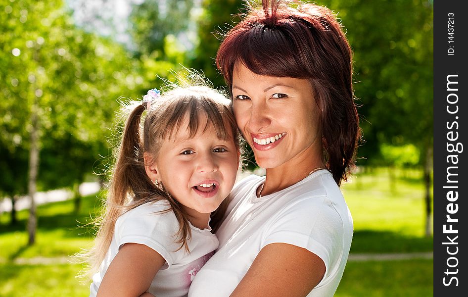 Happy young mother in park with her beautiful small daughter, both smiling and looking in camera. Happy young mother in park with her beautiful small daughter, both smiling and looking in camera