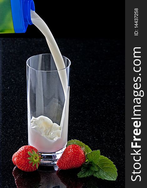 Milk pouring in glass with strawberries and mint leaves. Milk pouring in glass with strawberries and mint leaves