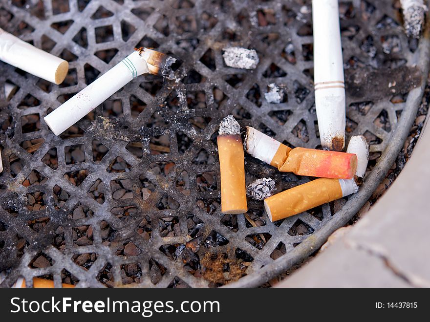 A dirty ashtray with smoked cigarette filters and butts with lipstick on them. A dirty ashtray with smoked cigarette filters and butts with lipstick on them