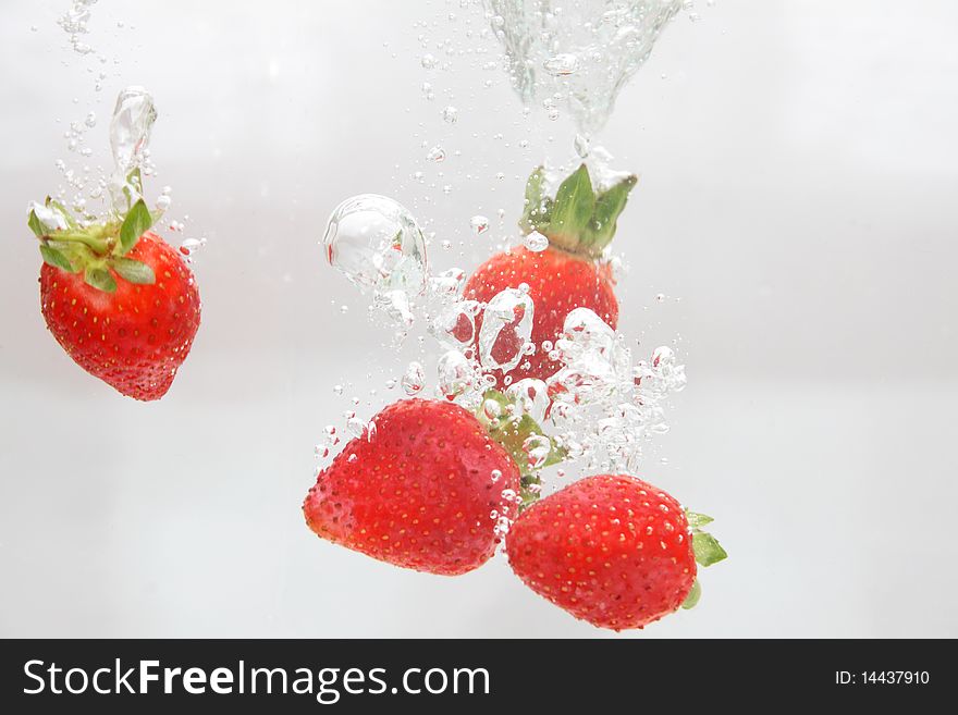 Five strawberries falling in water.