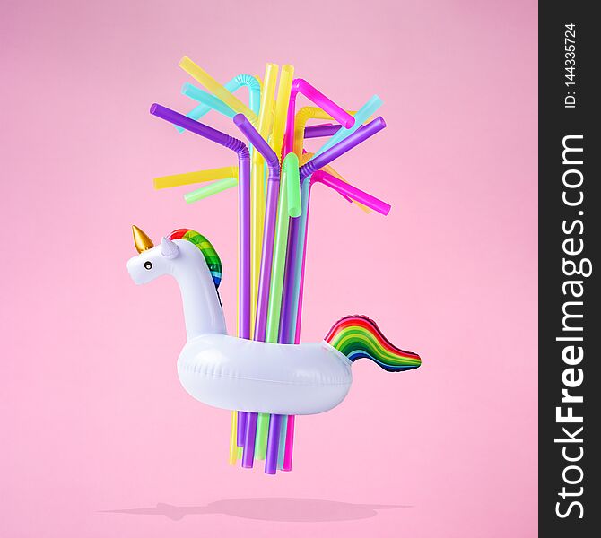 Colorful drinking straws with inflatable unicorn pool toy on pink background. Creative minimal summer concept