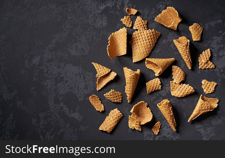 Crushed waffle ice cream cones on a black background, top view with copy space scoops summer dessert delicious sweet cold flavor tasty fresh sundae frozen snack dairy refreshment wafer empty calorie cool yummy colorful concept wooden cornet overhead gelato variety milk confection refreshing crisp thirst unhealthy
